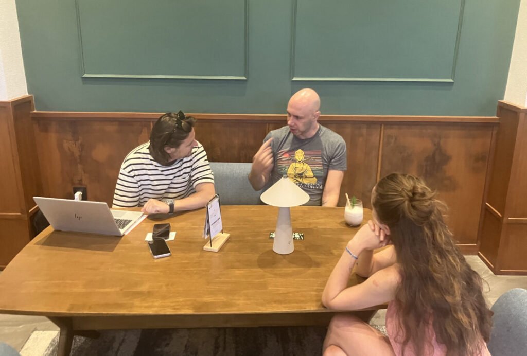 Three individuals seated at a table, each using a laptop, engaged in a collaborative work session.